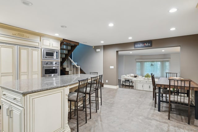 98 Beach Rd, Westhampton Beach, NY 11978 - kitchen featuring appliances with stainless steel finishes, cream cabinets, recessed lighting, light stone counters, and a kitchen bar