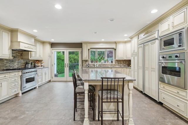 98 Beach Rd, Westhampton Beach, NY 11978 - kitchen featuring cream cabinets, built in appliances, custom range hood, tasteful backsplash, and light stone countertops