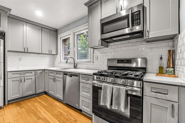 16 Rollhaus Pl, Port Chester, NY 10573 - kitchen featuring stainless steel appliances, gray cabinets, a sink, tasteful backsplash, and light wood-style flooring