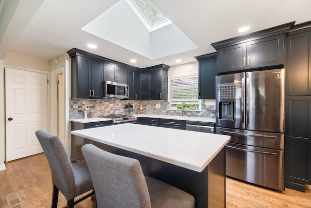 22 Willow Pl, Middletown, NY 10940 - kitchen featuring appliances with stainless steel finishes, a skylight, light stone countertops, a kitchen breakfast bar, and light wood-style flooring