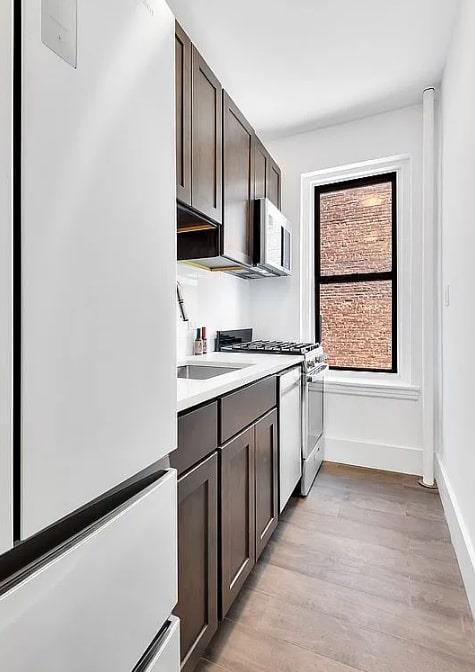 3000 Valentine Ave Unit 2E, Bronx, NY 10458 - kitchen featuring white appliances, dark brown cabinets, light wood finished floors, and a sink