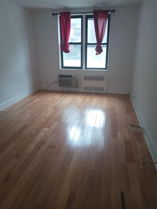 spare room with radiator heating unit, hardwood / wood-style flooring, an AC wall unit, and baseboards