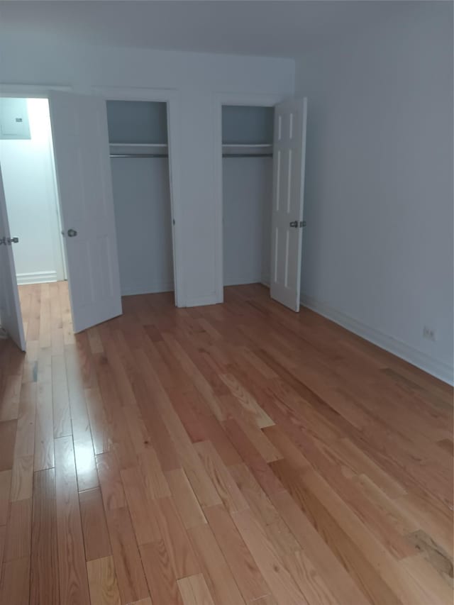unfurnished bedroom with two closets, light wood-style floors, and baseboards
