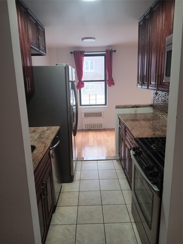 kitchen with radiator heating unit, appliances with stainless steel finishes, light stone counters, light tile patterned flooring, and dark brown cabinets