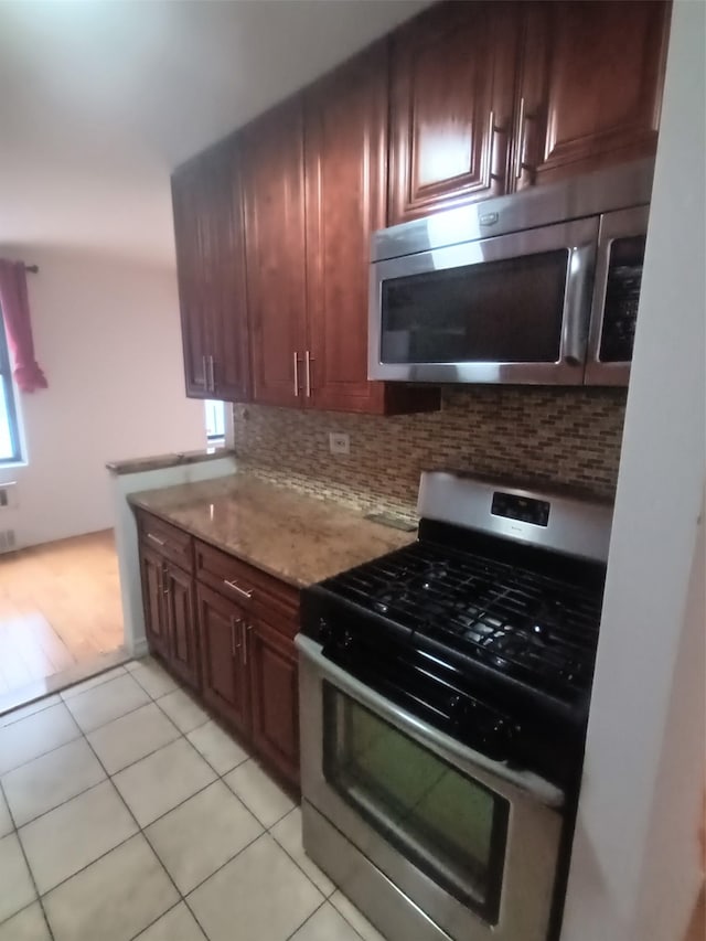 kitchen with stainless steel appliances, decorative backsplash, light tile patterned flooring, and light stone countertops