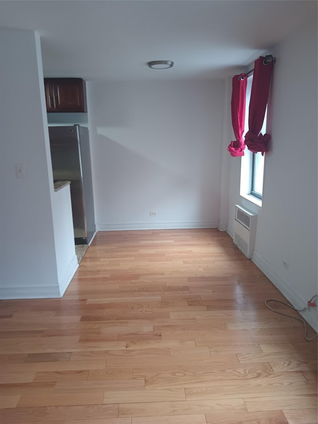 spare room featuring radiator heating unit, light wood-type flooring, and baseboards