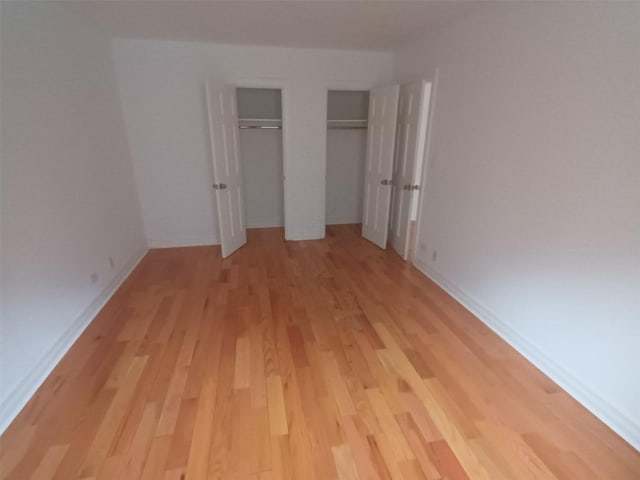 unfurnished bedroom with light wood-style floors, two closets, and baseboards