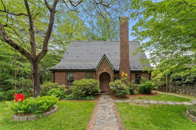 tudor-style house with brick siding, a high end roof, a chimney, and a front yard