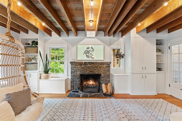 sitting room featuring light wood finished floors, beam ceiling, a stone fireplace, and wood ceiling