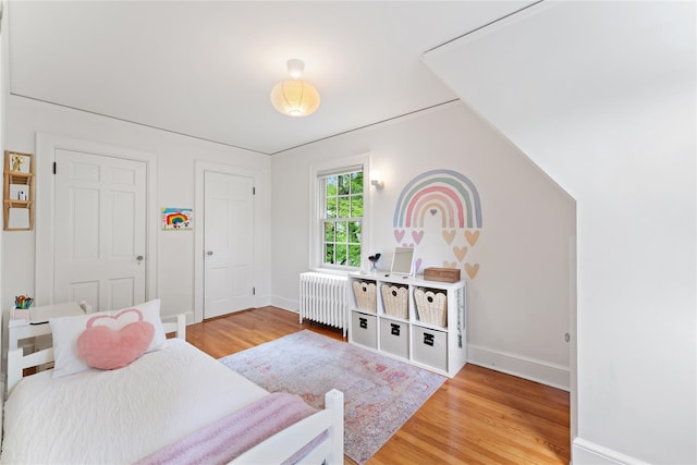 bedroom with radiator heating unit, light wood-type flooring, and baseboards