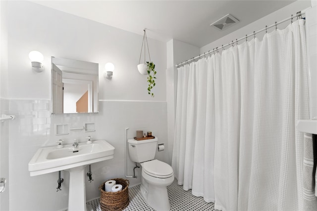 bathroom featuring toilet, tile walls, wainscoting, and a shower with shower curtain