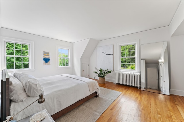 bedroom with radiator heating unit, light wood finished floors, and baseboards