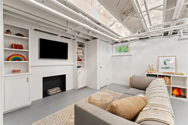 living area featuring concrete flooring, baseboards, a fireplace, and built in shelves