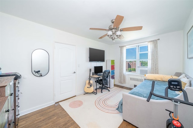 bedroom with radiator heating unit, wood finished floors, baseboards, and a desk