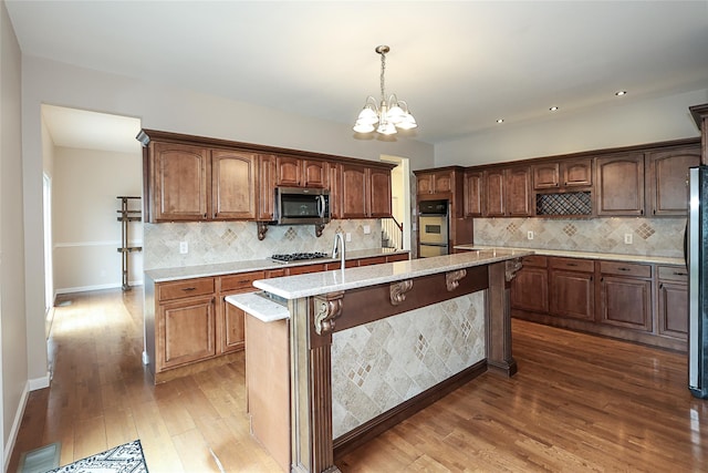 114 Frankel Blvd, Merrick, NY 11566 - kitchen with stainless steel appliances, a chandelier, hardwood / wood-style flooring, a center island with sink, and decorative backsplash