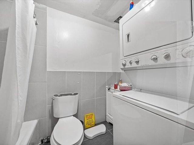 36 Starr Ave, Monticello, NY 12701 - full bathroom featuring stacked washer / dryer, toilet, tile patterned floors, tile walls, and a wainscoted wall