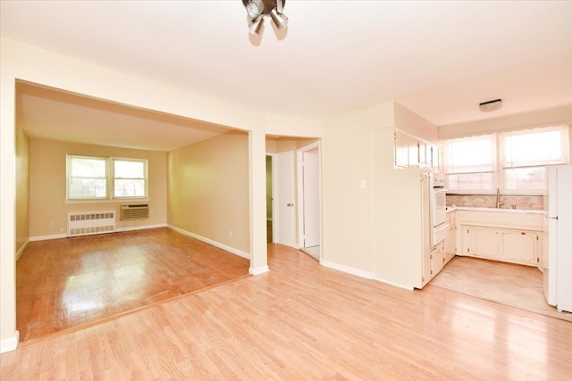 unfurnished living room featuring radiator heating unit, light wood-style floors, and baseboards