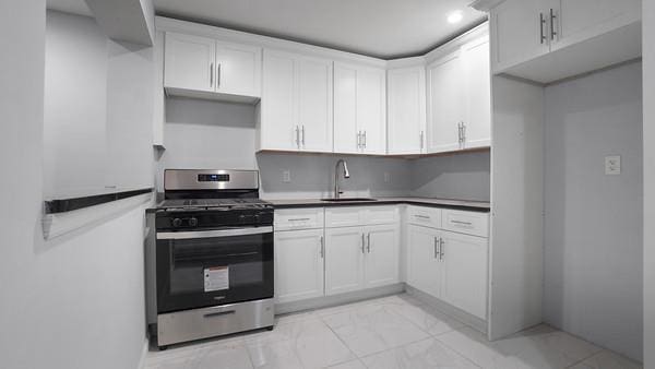 2040 Washington Ave, Bronx, NY 10457 - kitchen featuring gas stove, a sink, freestanding refrigerator, light marble finish floors, and white cabinetry