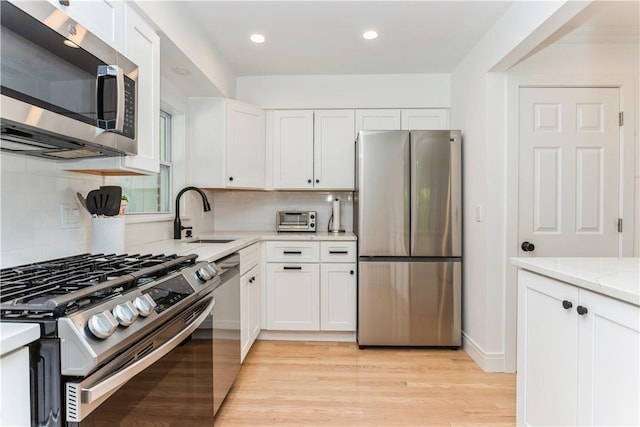 kitchen with appliances with stainless steel finishes, a sink, white cabinets, light wood finished floors, and decorative backsplash