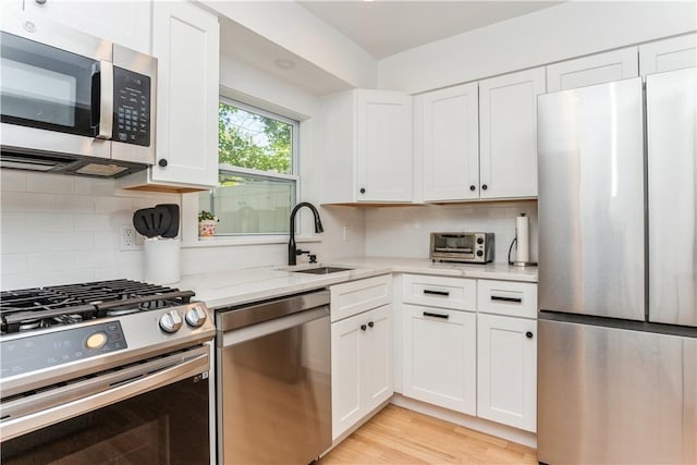kitchen with appliances with stainless steel finishes, a sink, light stone counters, white cabinetry, and tasteful backsplash