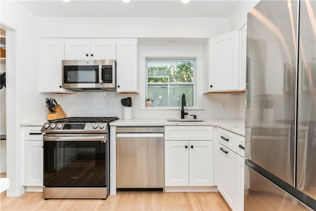 kitchen with stainless steel appliances, a sink, light wood-type flooring, backsplash, and white cabinetry