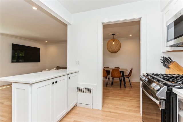 kitchen featuring range with gas stovetop, stainless steel microwave, white cabinets, crown molding, and light wood-style flooring
