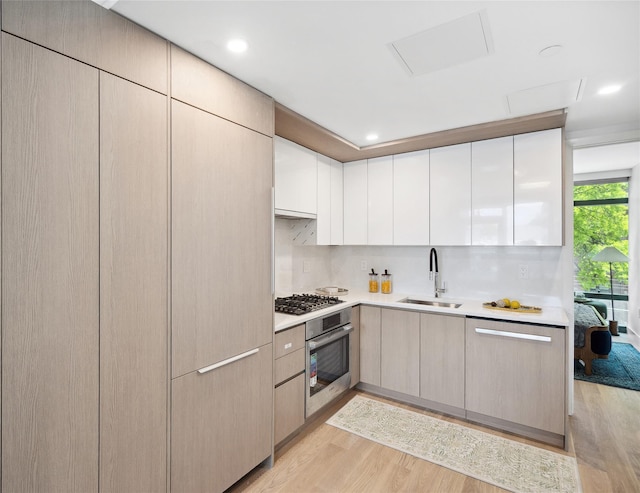 kitchen featuring a sink, appliances with stainless steel finishes, light wood-style flooring, light countertops, and recessed lighting