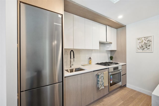 kitchen featuring stainless steel appliances, a sink, light countertops, light wood-type flooring, and white cabinetry