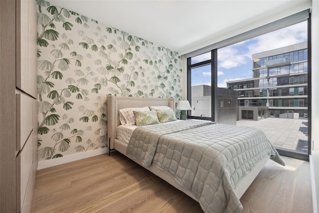 bedroom featuring wallpapered walls, baseboards, wood finished floors, an accent wall, and floor to ceiling windows
