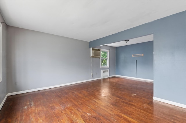 spare room with radiator heating unit, baseboards, wood finished floors, and a wall mounted air conditioner