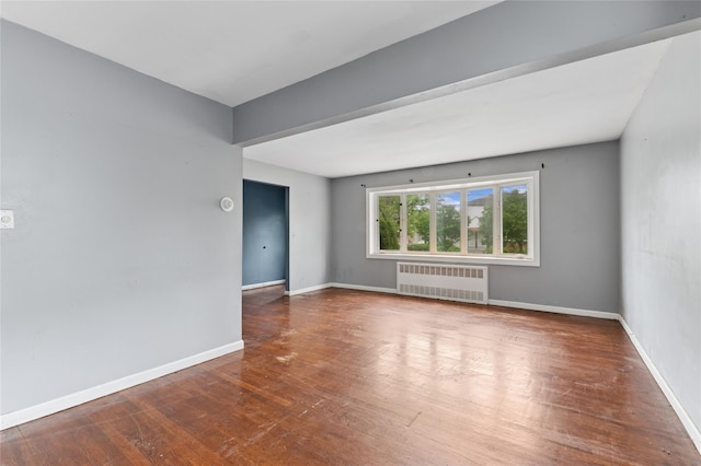 empty room with radiator, wood finished floors, and baseboards