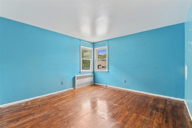 unfurnished room featuring radiator heating unit, hardwood / wood-style floors, and baseboards