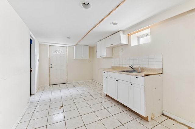 kitchen featuring a sink, tasteful backsplash, white cabinets, light tile patterned floors, and light countertops
