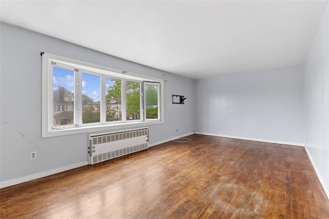 empty room with radiator, hardwood / wood-style flooring, and baseboards
