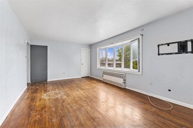 empty room featuring radiator heating unit, hardwood / wood-style flooring, and baseboards