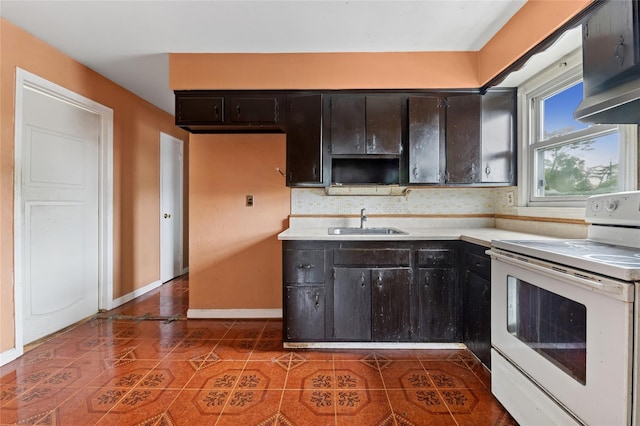 kitchen with electric range, a sink, light countertops, baseboards, and dark tile patterned flooring