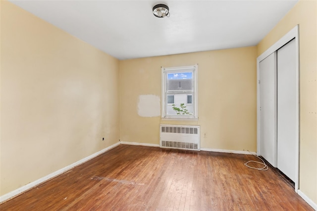 unfurnished bedroom featuring radiator heating unit, wood-type flooring, baseboards, and a closet