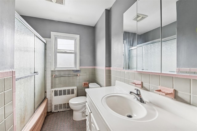 bathroom featuring radiator heating unit, toilet, tile walls, vanity, and combined bath / shower with glass door