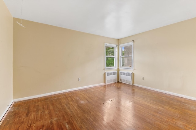 empty room with radiator heating unit, wood finished floors, and baseboards
