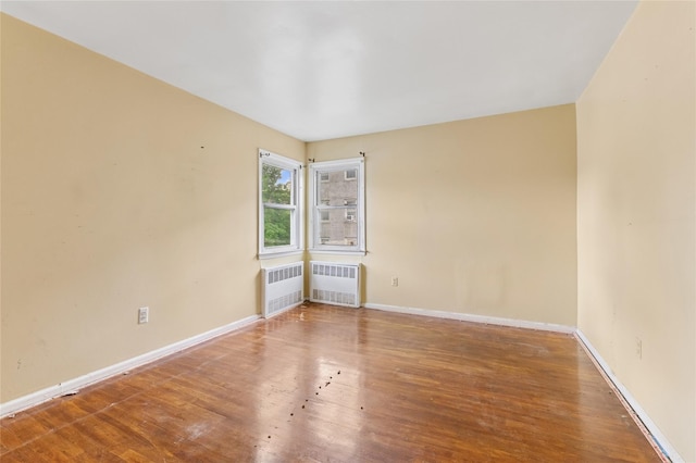 spare room featuring radiator, wood finished floors, and baseboards