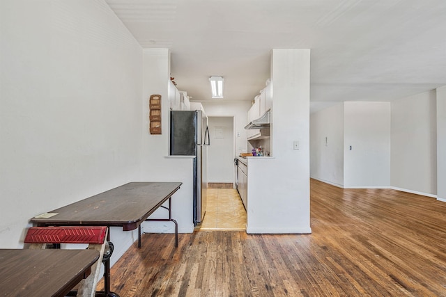 190 W Merrick Rd Unit 4E, Freeport, NY 11520 - kitchen featuring light wood-type flooring, white cabinets, freestanding refrigerator, under cabinet range hood, and light countertops