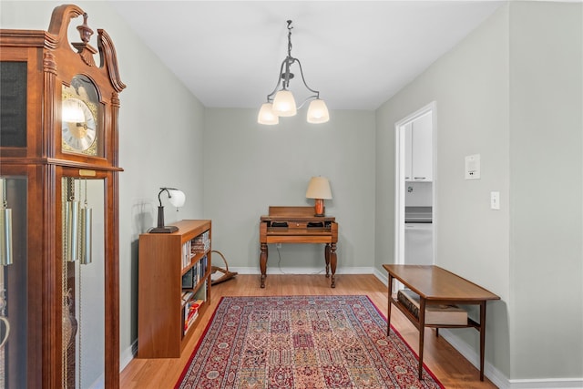 hall featuring light wood-style floors, a chandelier, and baseboards
