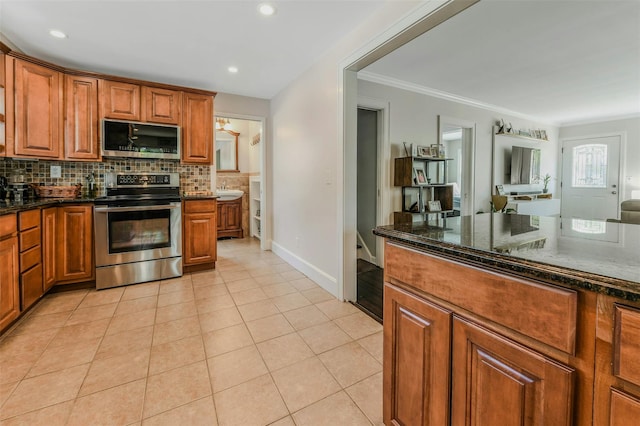935 Harrison Dr, Centerport, NY 11721 - kitchen with appliances with stainless steel finishes, brown cabinetry, tasteful backsplash, light tile patterned floors, and ornamental molding
