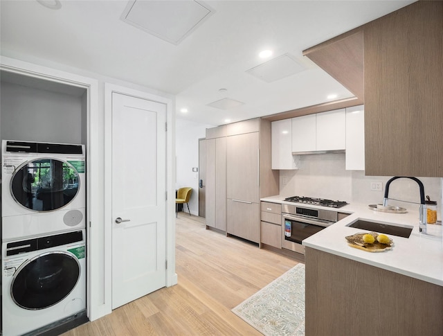 kitchen with stainless steel appliances, stacked washing machine and dryer, a sink, light countertops, and white cabinetry