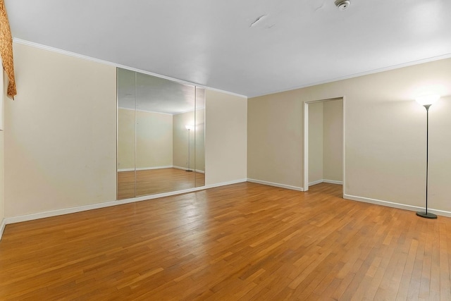 empty room featuring light wood-type flooring, baseboards, and ornamental molding
