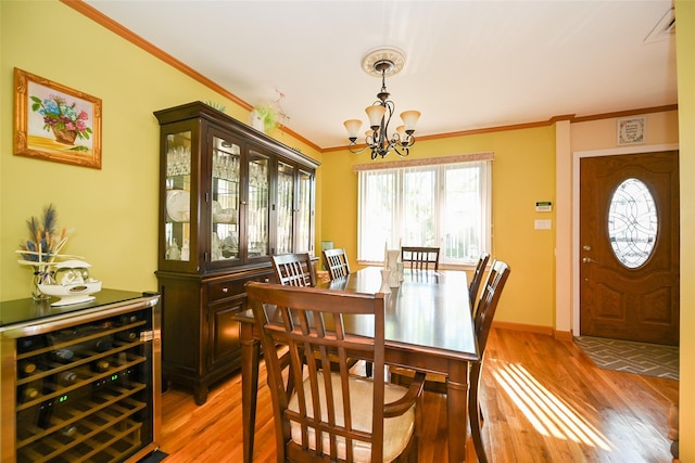 dining area featuring beverage cooler, crown molding, light wood-style flooring, a chandelier, and baseboards