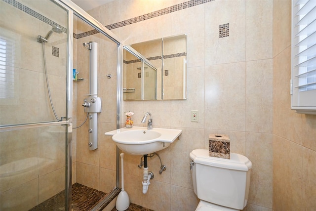 full bath with tile walls, toilet, a stall shower, and a sink