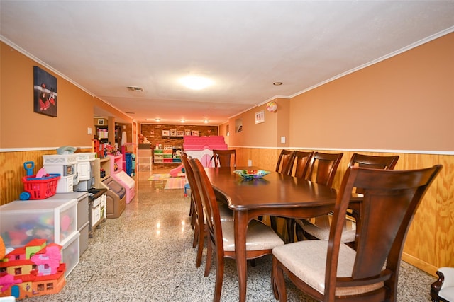 dining area featuring wainscoting, wooden walls, and crown molding