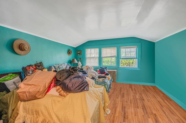 bedroom with radiator heating unit, wood finished floors, lofted ceiling, baseboards, and crown molding