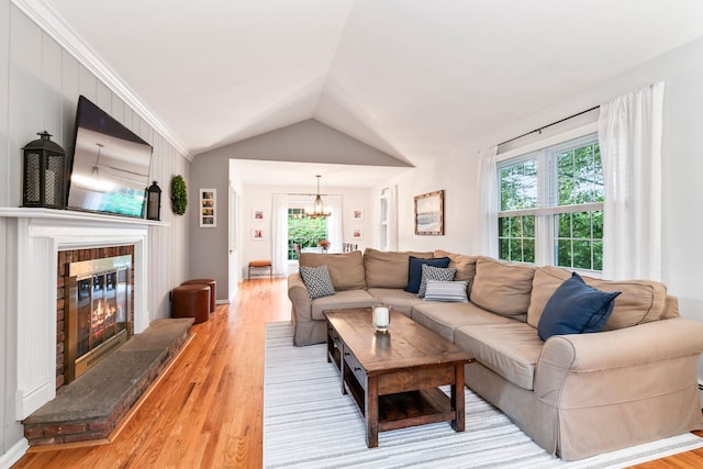 living area with a fireplace, a chandelier, light wood-style flooring, and vaulted ceiling